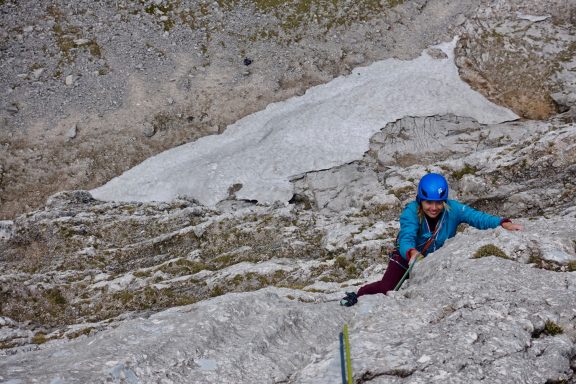 Kletterer in blauer Jacke und Helm, der an einer steilen Felswand hochklettert.