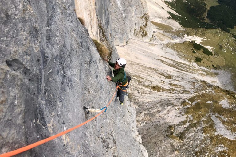 Ein Kletterer, der eine steile Felswand erklimmt, gesichert mit einem Seil.