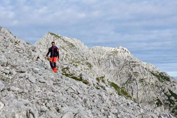 Wanderer auf einem felsigen Weg in bergiger Landschaft unter einem bewölkten Himmel.