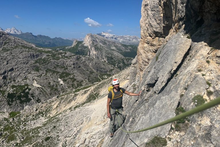Kletterer an steiler Felswand in den Bergen, umgeben von grüner Landschaft und Hochgebirge.