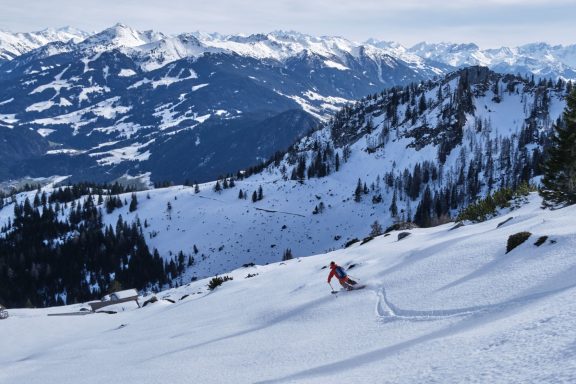 Skitouren Camp Rofan Skifahrer fährt über einen schneebedeckten Hang mit Bergen im Hintergrund.