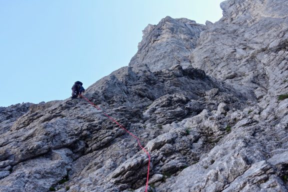 Kletterer sichert sich mit Seil an einer schroffen Felswand.