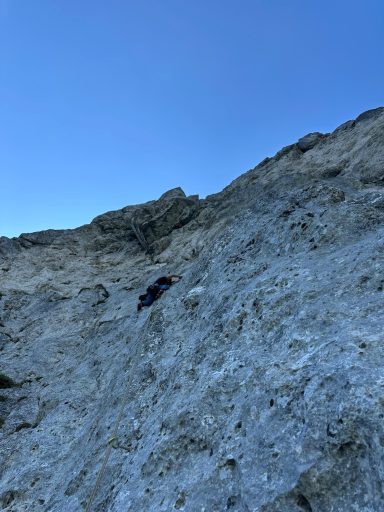 Kletterer bestiegt eine steile Felswand unter klarem blauen Himmel.