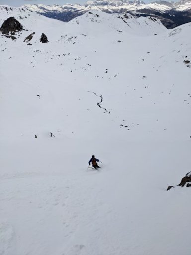 Skifahrer im verschneiten Gebirgstal, umgeben von schneebedeckten Bergen und Felsen.