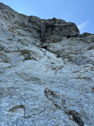 Steile Felswand mit Wasserfall und blassem Himmel im Hintergrund.