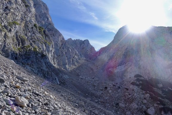 Hohe Bergfelsen unter einem klaren Himmel mit Sonnenstrahlen. Schotteriger Untergrund.