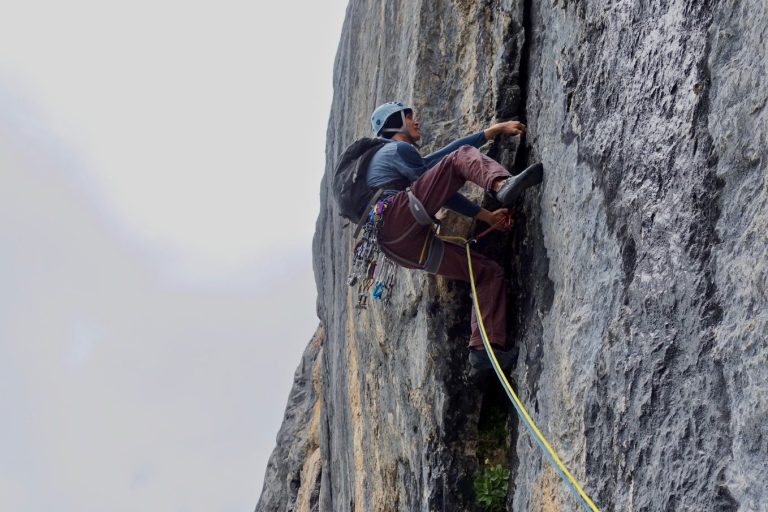 Ein Kletterer, der eine steile Felswand erklimmt, gesichert mit einem Seil.