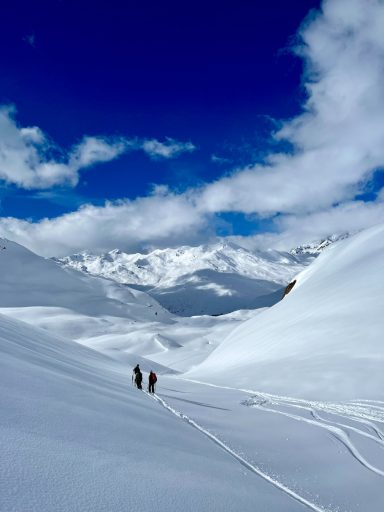 Zwei Wanderer im Schnee unter einem klaren blauen Himmel und beeindruckenden Bergen.