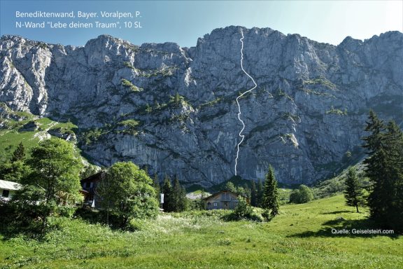 Grüne Wiese mit Bäumen und steil aufragenden Felsen im Hintergrund.