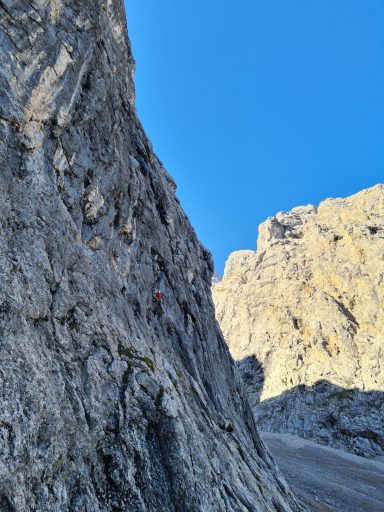 Kletterer an steiler Felswand unter blauem Himmel.