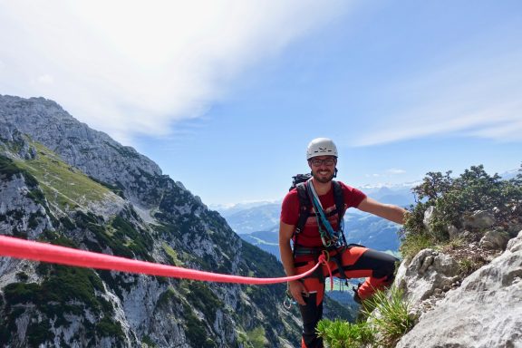 Kletterer sichert sich mit Seil in den Alpen, umgeben von Felsen und Bergen.