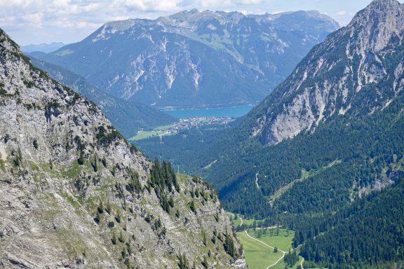 Berglandschaft mit steilen Felsen, grünen Wäldern und einem blauen See im Tal.