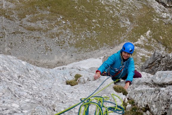 Kletterer in blauer Jacke und Helm, der an einem Felsen hochsteigt.