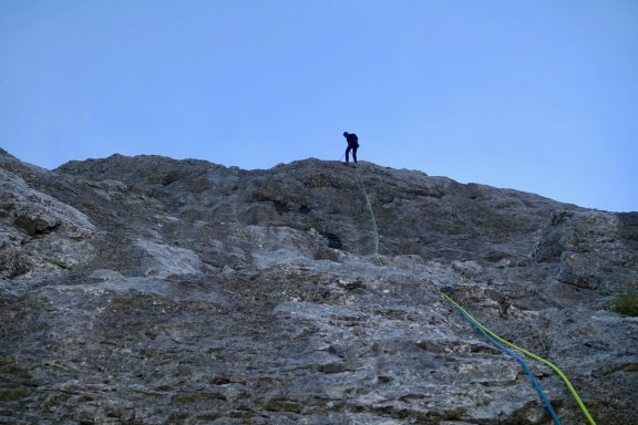 Kletterer am Felsen, Himmel im Hintergrund, Seil hängt herab.