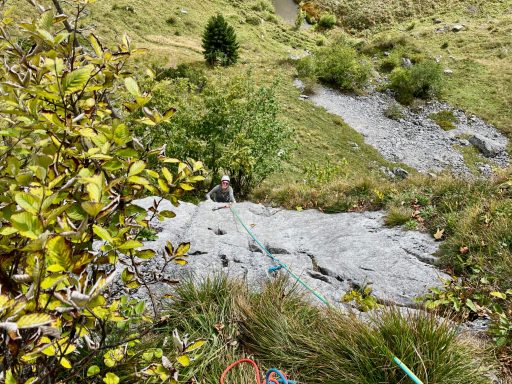 Klettersteig mit Seil in bergiger Landschaft, umgeben von Bäumen und Gras.