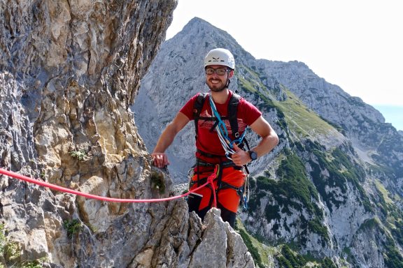 Kletterer auf einem Grat mit Seil, umgeben von bergiger Landschaft.