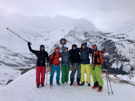 Gruppe von sechs Personen in Skikleidung auf einem schneebedeckten Berg.