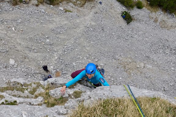 Kletterer in blauer Kleidung erklimmt steilen Felsen mit einem Seil.