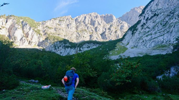 Mann mit Helm geht in ein von hohen Bergen umgebenes Tal.