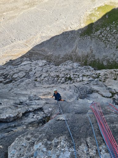 Kletterer, der auf steiniger Felswand in den Bergen klettert. Seil und Ausrüstung sichtbar.