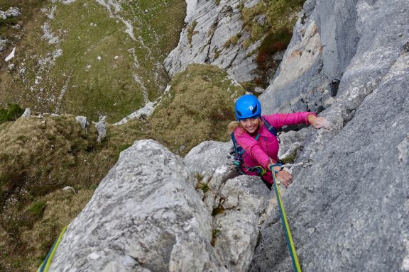 Kletterer in pinkem Outfit, der an einer senkrechten Felswand hochsteigt.