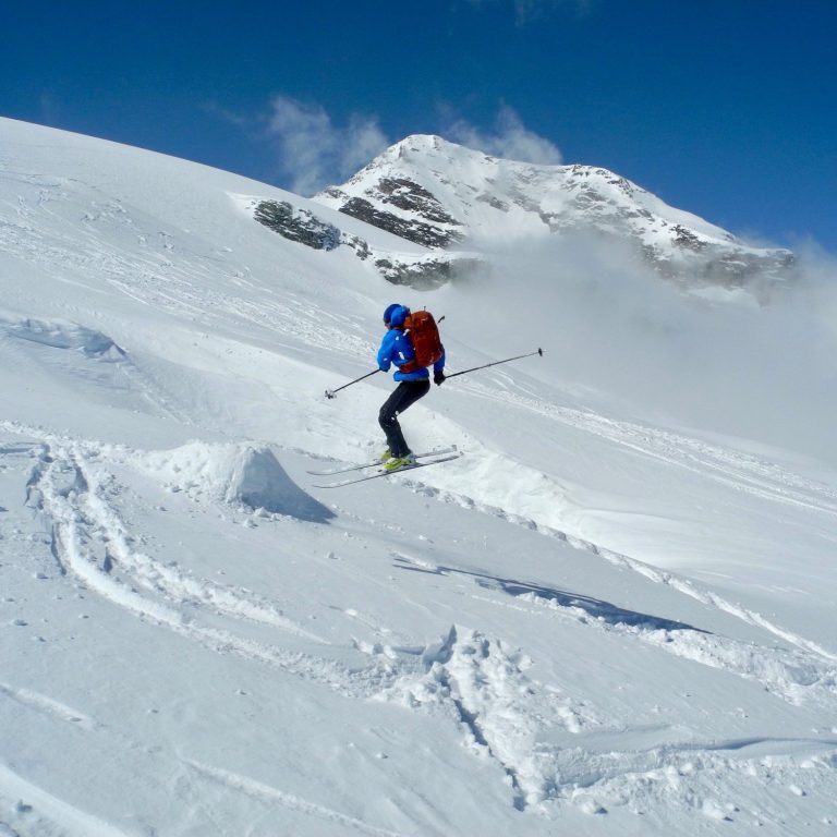 Skifahrer springt über eine Schneehügel in bergiger Winterlandschaft.