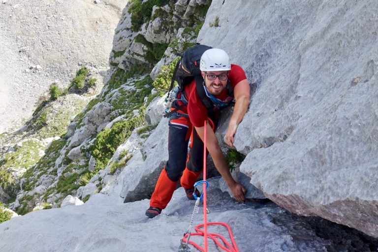 Ein Kletterer, der eine steile Felswand erklimmt, gesichert mit einem Seil.