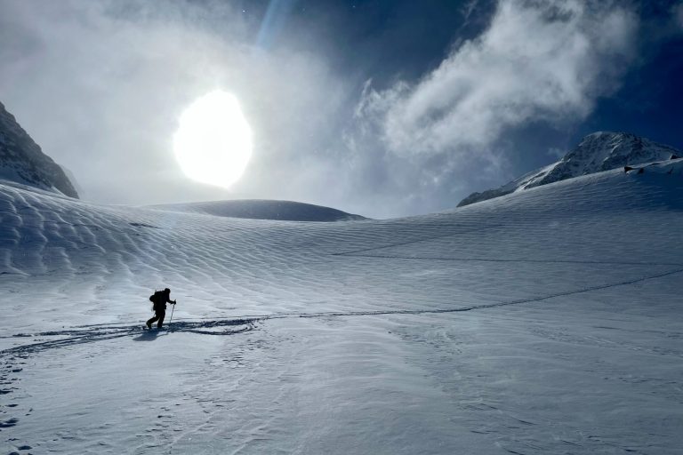 Ein Skifahrer durchquert eine unberührte, schneebedeckte Landschaft unter klarem Himmel.
