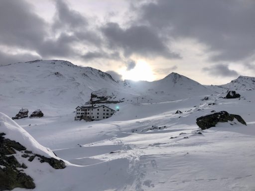Schneebedeckte Landschaft mit Bergen und einem Gebäude im Hintergrund, Sonnenstrahlen sehen aus.
