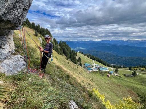 Person beim Klettern an einem Felsen mit bergiger Landschaft im Hintergrund.