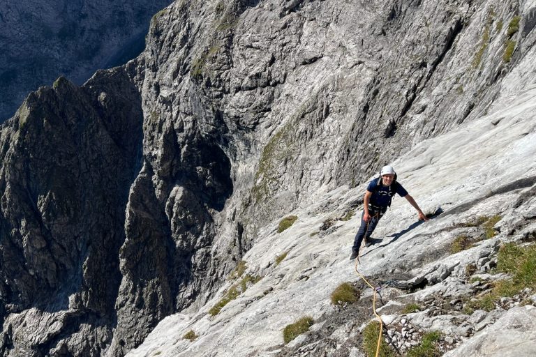 Kletterer erklimmt steile Felswand in bergiger Umgebung.