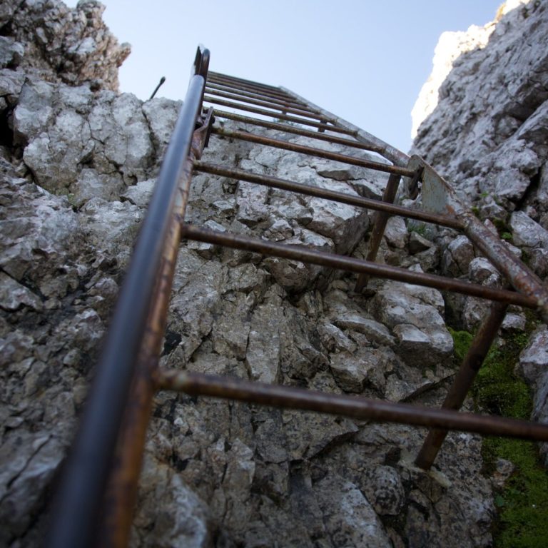 Eisenleiter, die an einer Felswand nach oben führt, unter blauem Himmel.